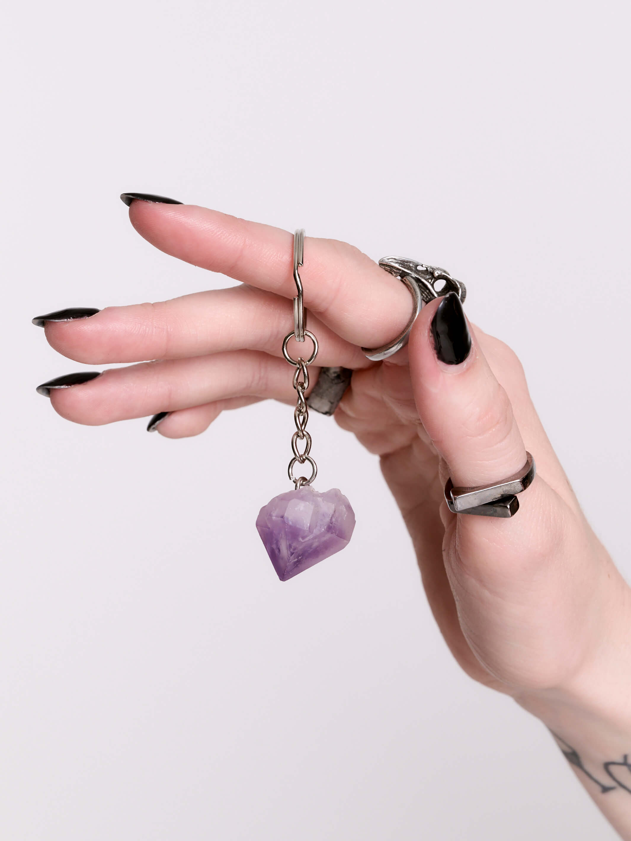 A silver keychain featuring a small purple amethyst crystal against a light gray background.