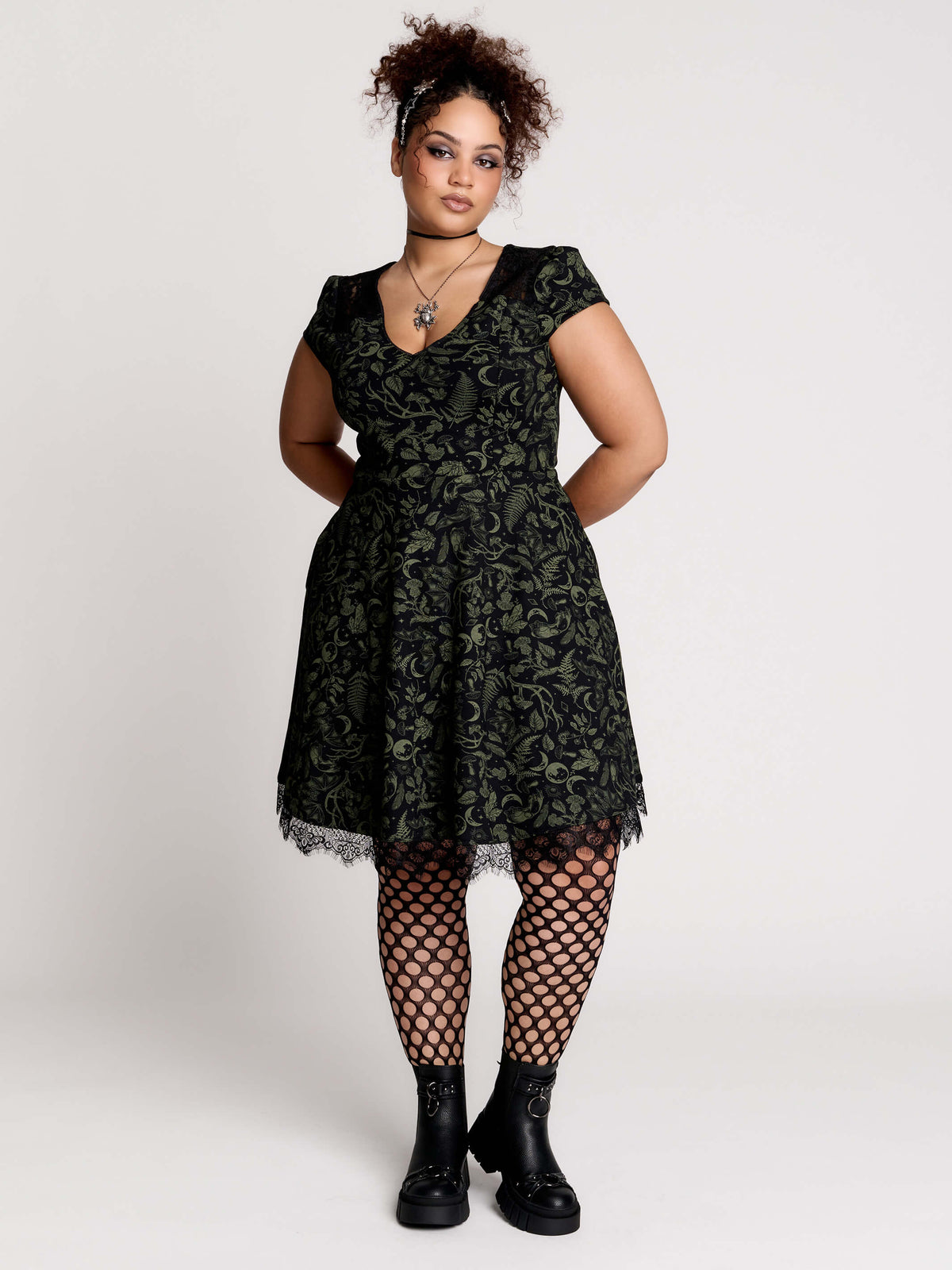 short black dress with a green leafy lace pattern, featuring cap sleeves, a V-neckline, side pockets, and a scalloped lace hem.