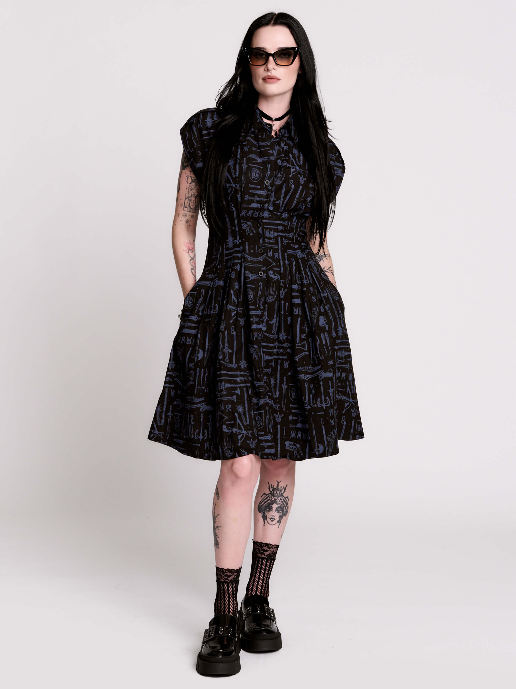 a button-front shirt dress featuring a striking medieval-inspired print with weaponry and macabre motifs.