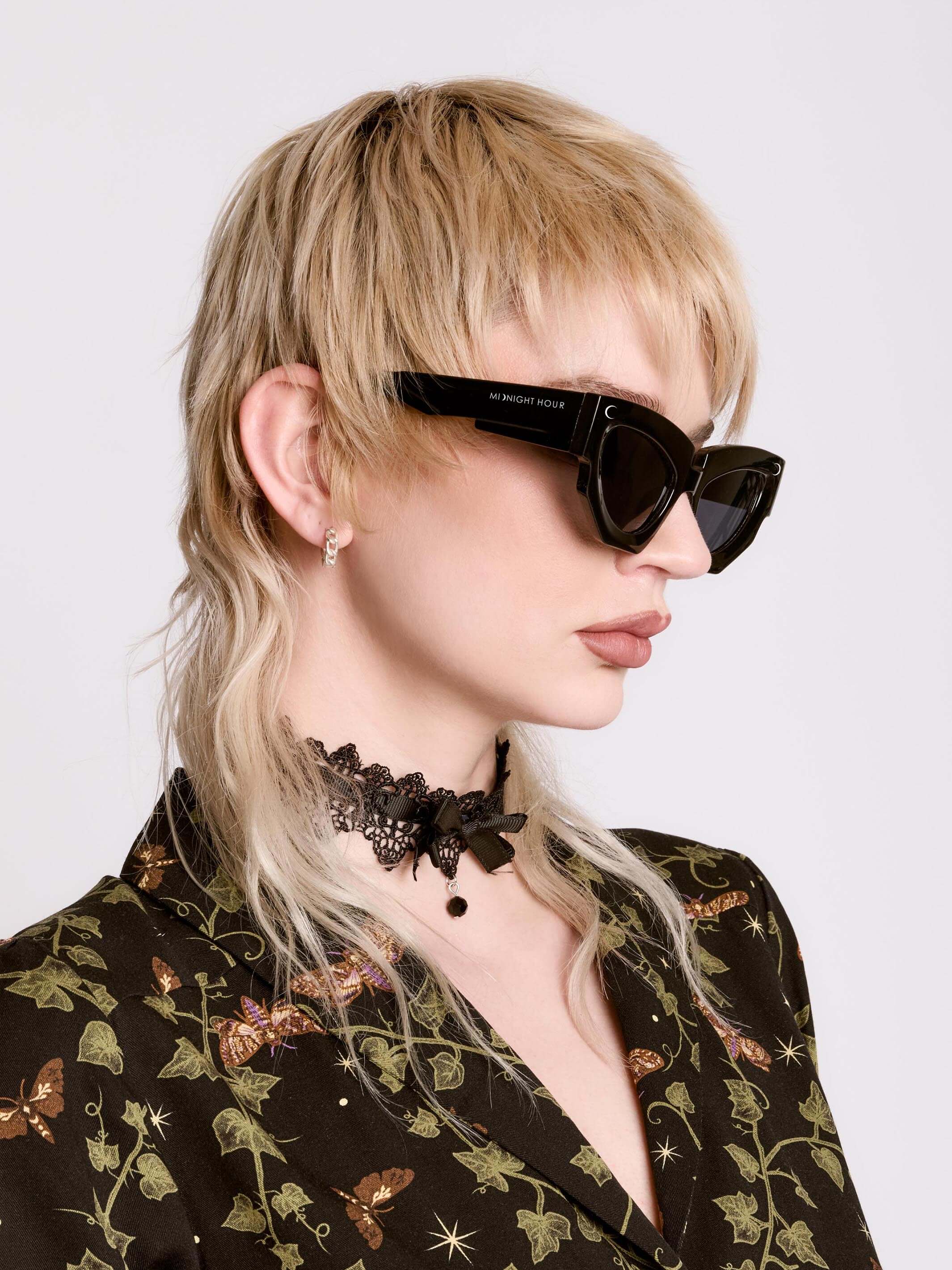 A person wearing black sunglasses with a unique shape, featuring a logo on the side and crescent moon on the front.