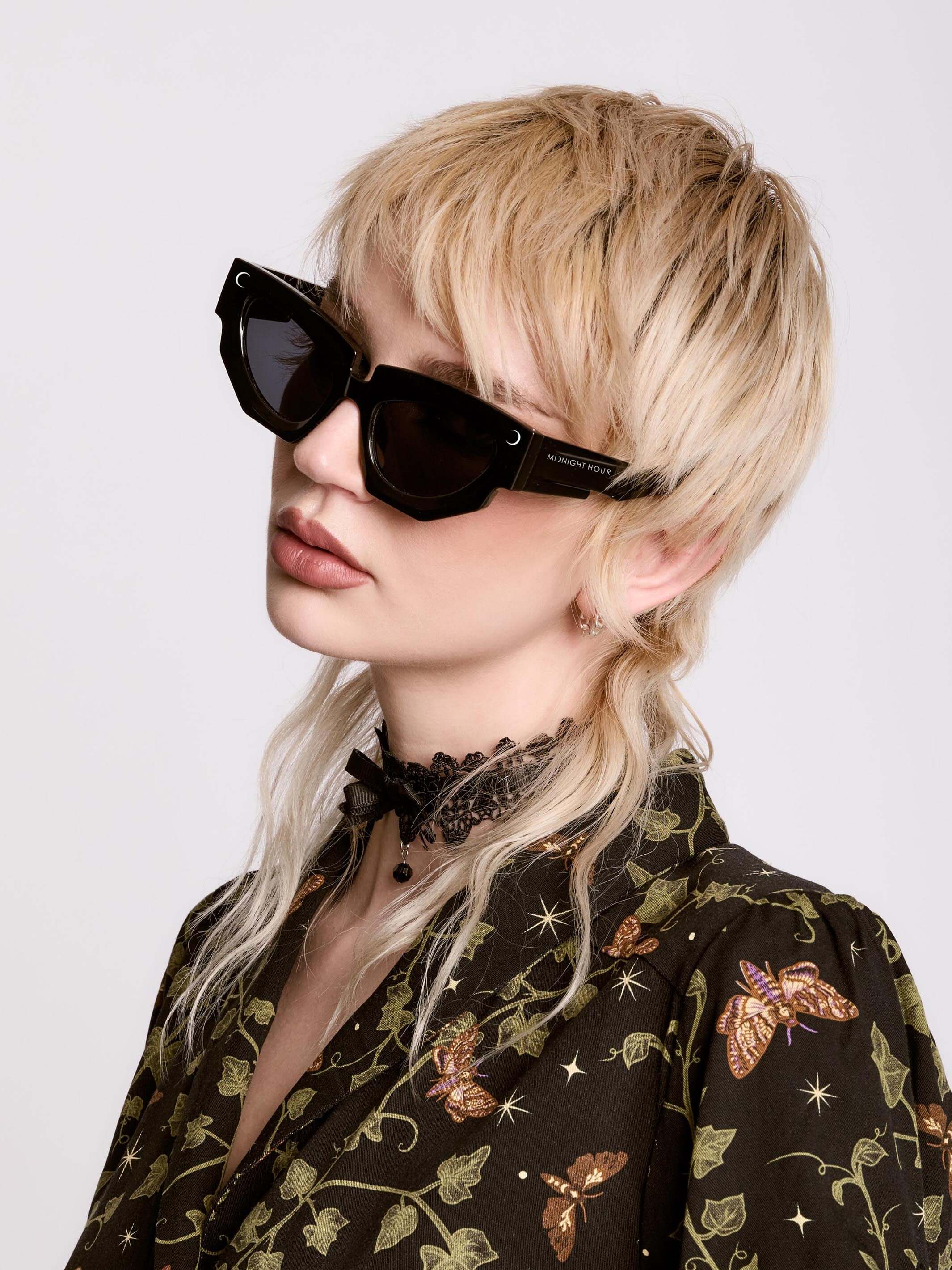 Person with short blonde hair and sunglasses on a white background
