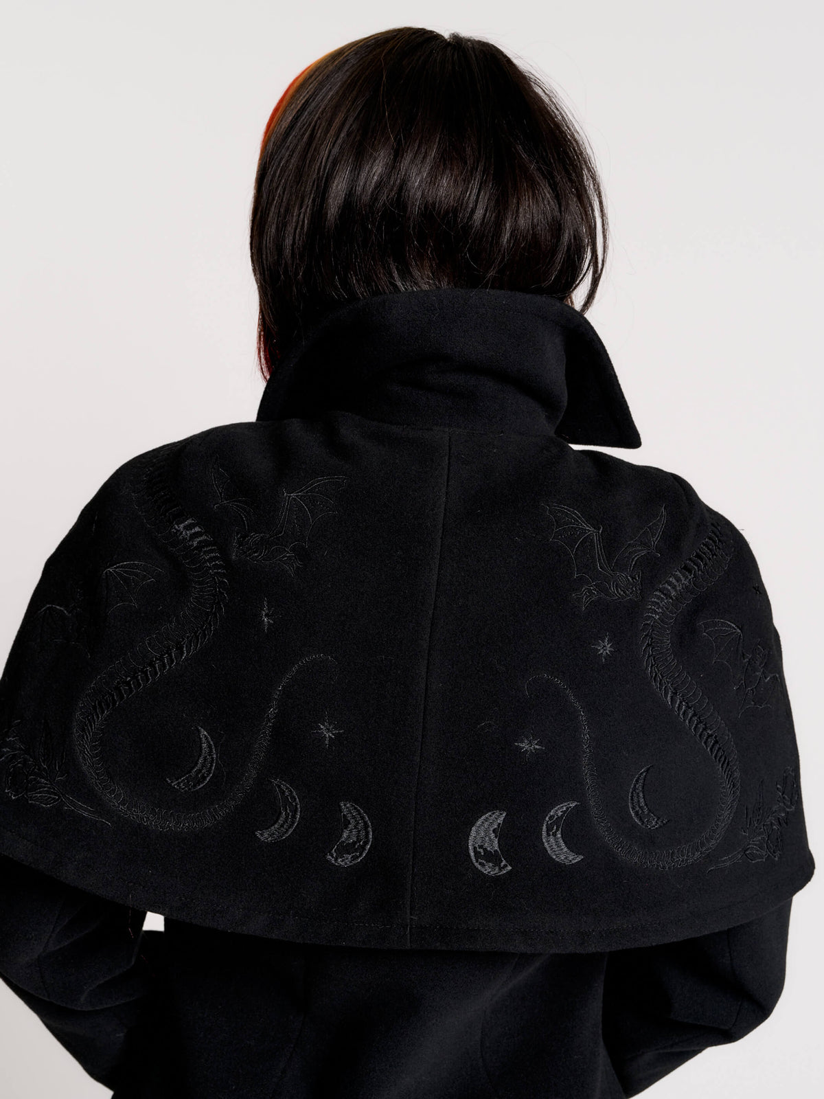 a black double-breasted coat with silver buttons and gothic dragon embroidery on the shoulder cape