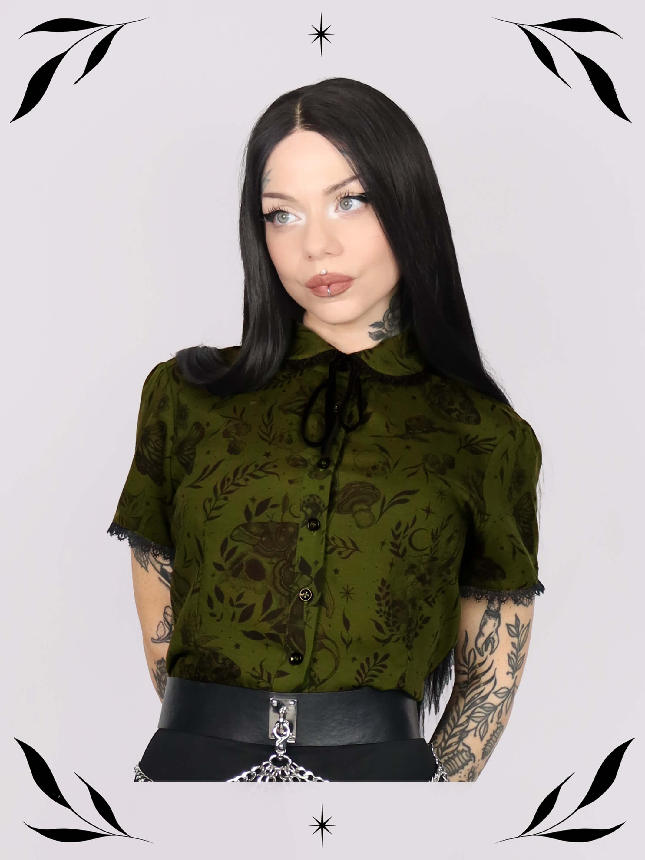 a short-sleeve olive green blouse with a dark botanical pattern, black lace trim collar with black ribbon tie detail and black buttons.