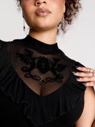 a black sheer mock-neck top with a black graphic on the chest