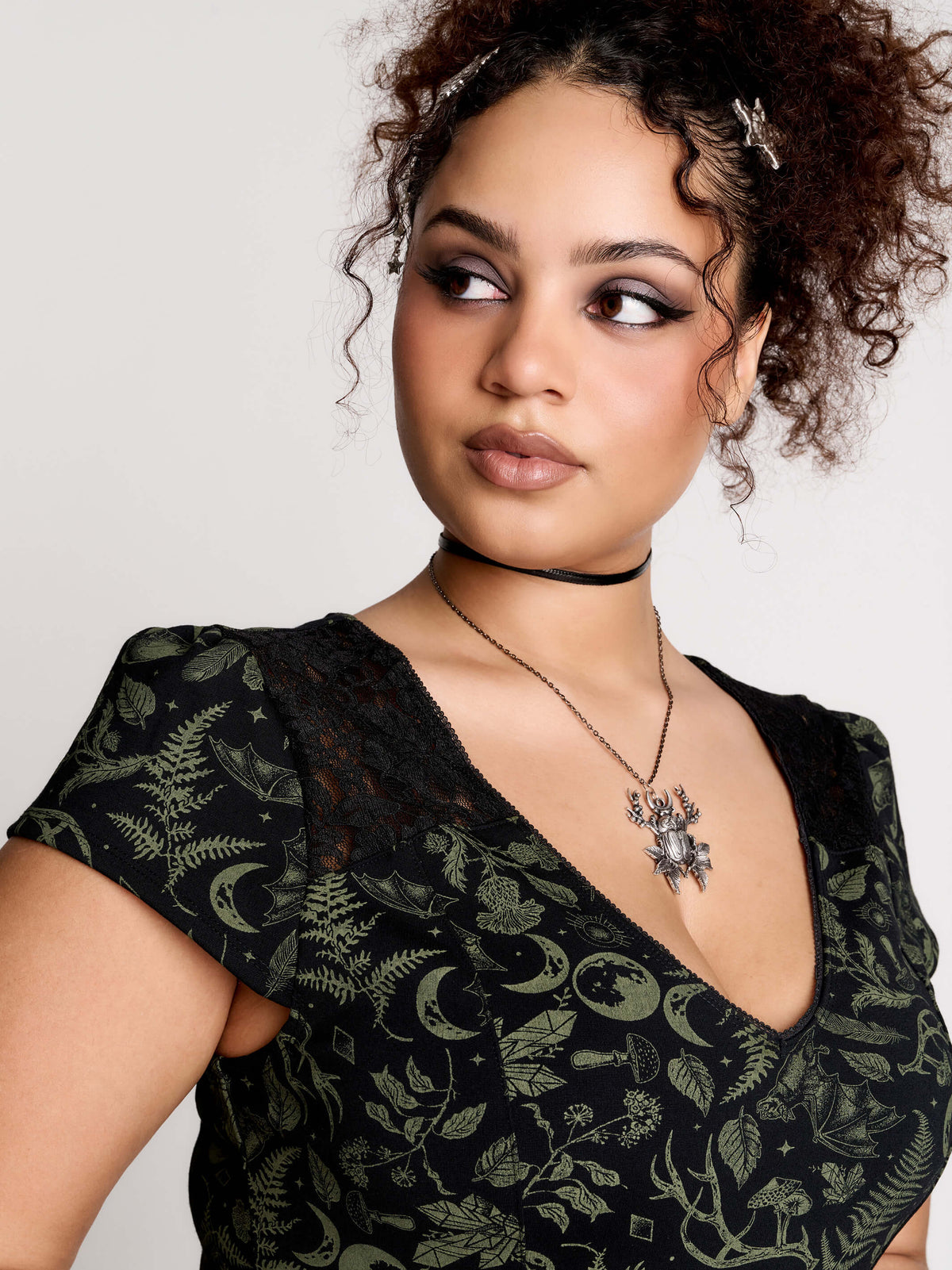 short black dress with a green leafy lace pattern, featuring cap sleeves, a V-neckline, side pockets, and a scalloped lace hem.