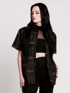 a black short-sleeve button-up shirt with a dark green and pink occult-style pattern.