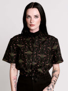 a black short-sleeve button-up shirt with a dark green and pink occult-style pattern.