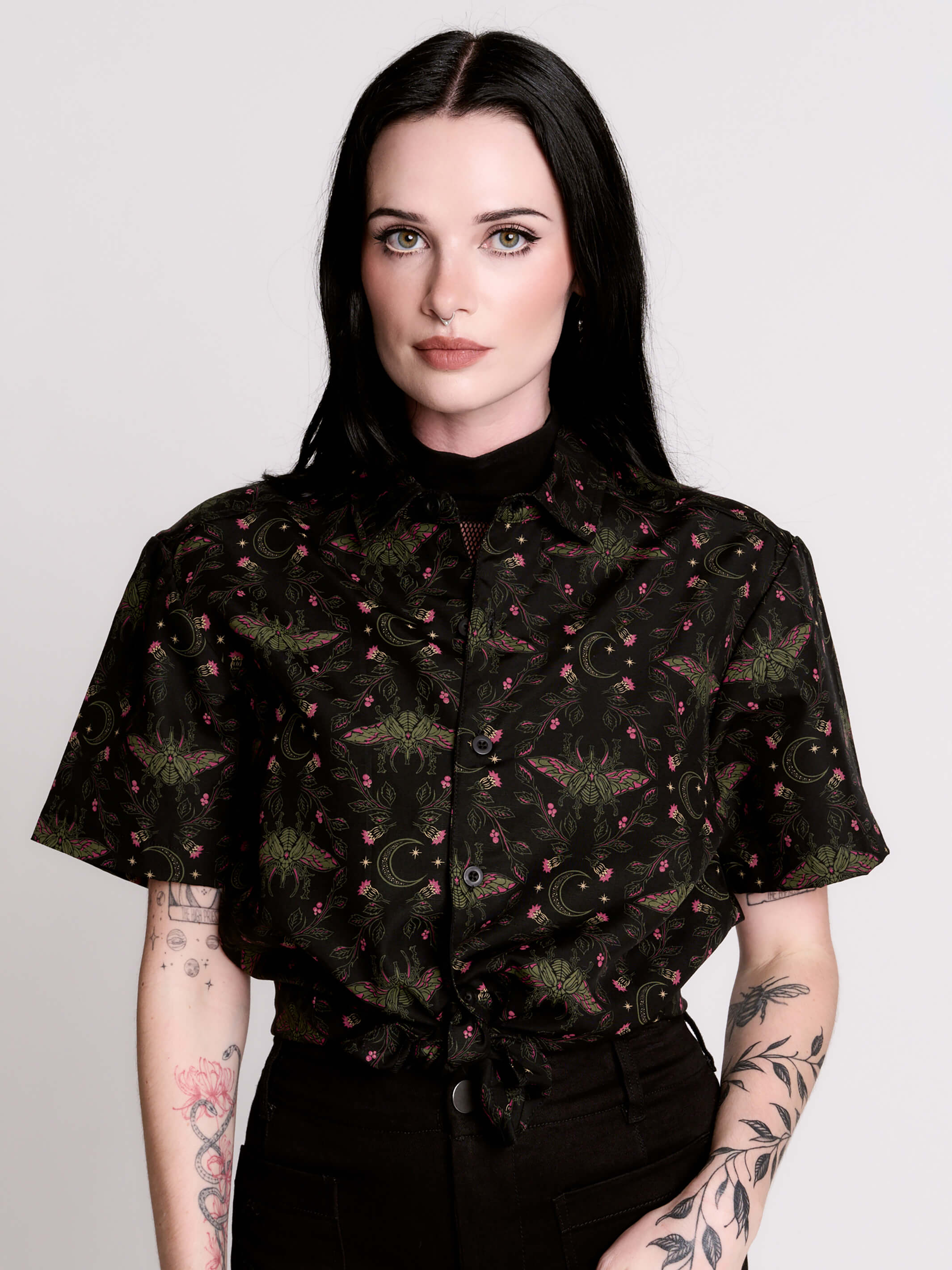 a black short-sleeve button-up shirt with a dark green and pink occult-style pattern.