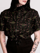 a black short-sleeve button-up shirt with a dark green and pink occult-style pattern.