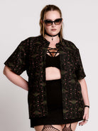 a black short-sleeve button-up shirt with a dark green and pink occult-style pattern.