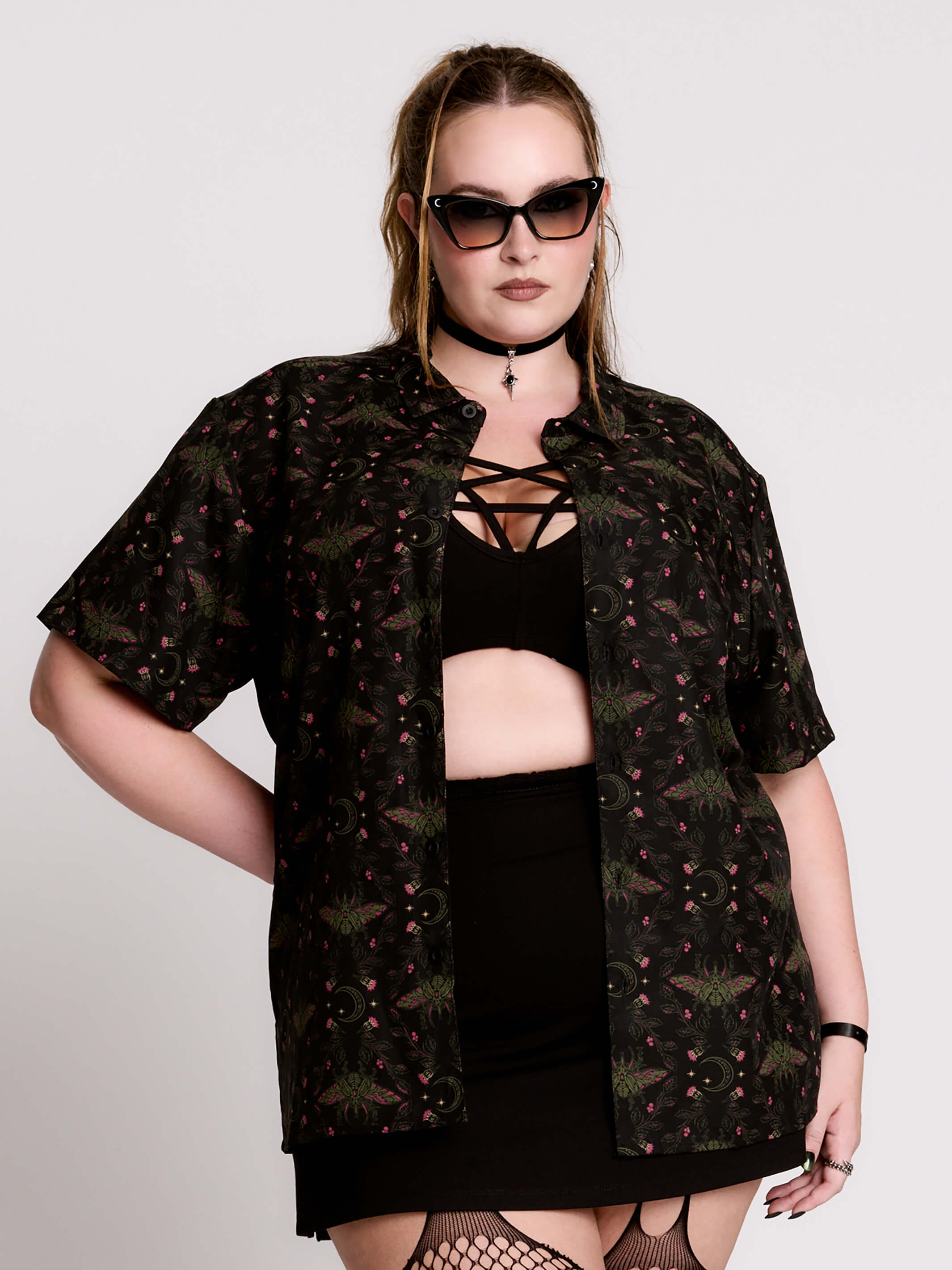 a black short-sleeve button-up shirt with a dark green and pink occult-style pattern.