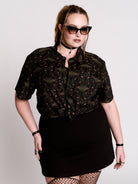 a black short-sleeve button-up shirt with a dark green and pink occult-style pattern.
