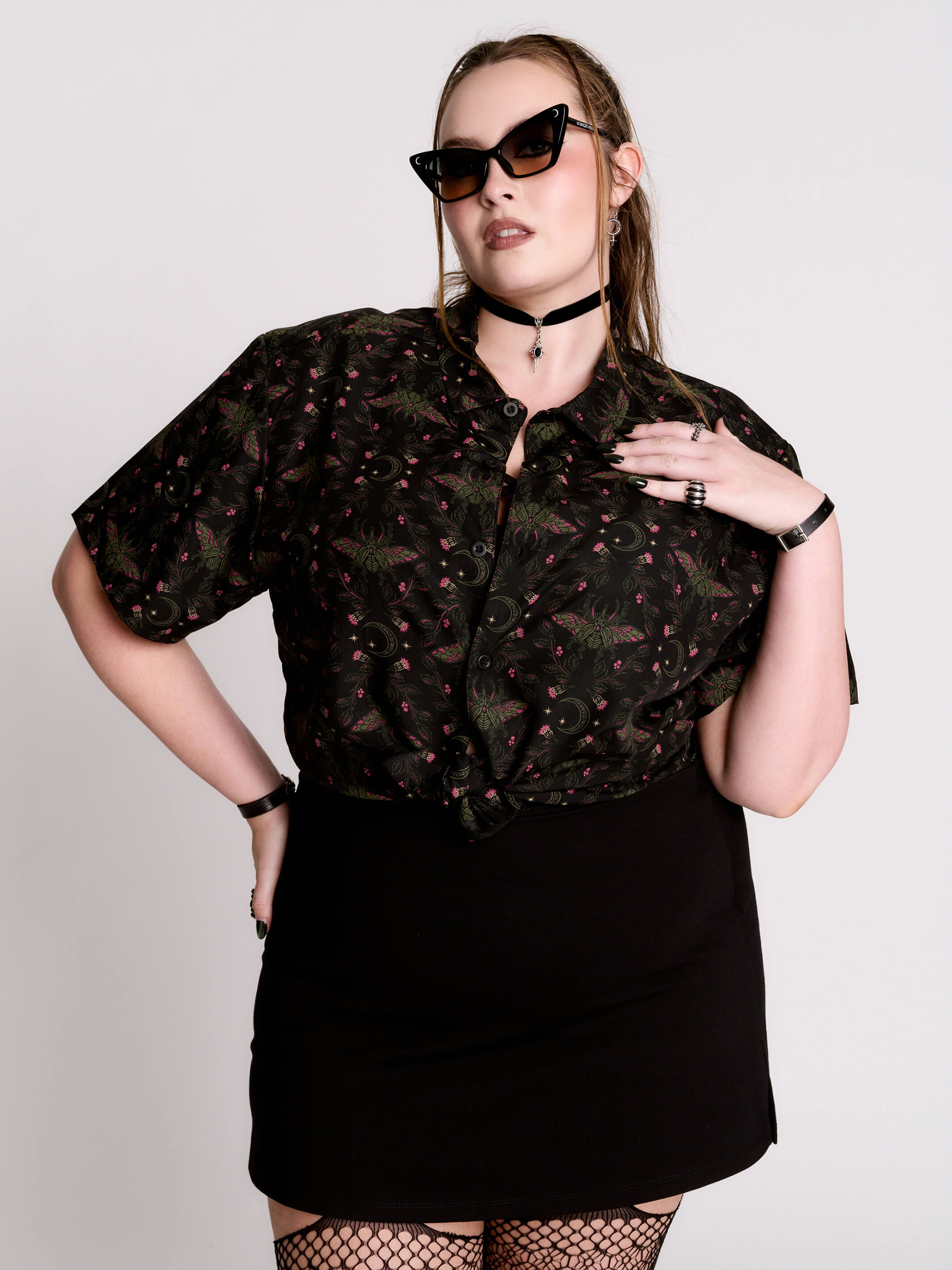 a black short-sleeve button-up shirt with a dark green and pink occult-style pattern.