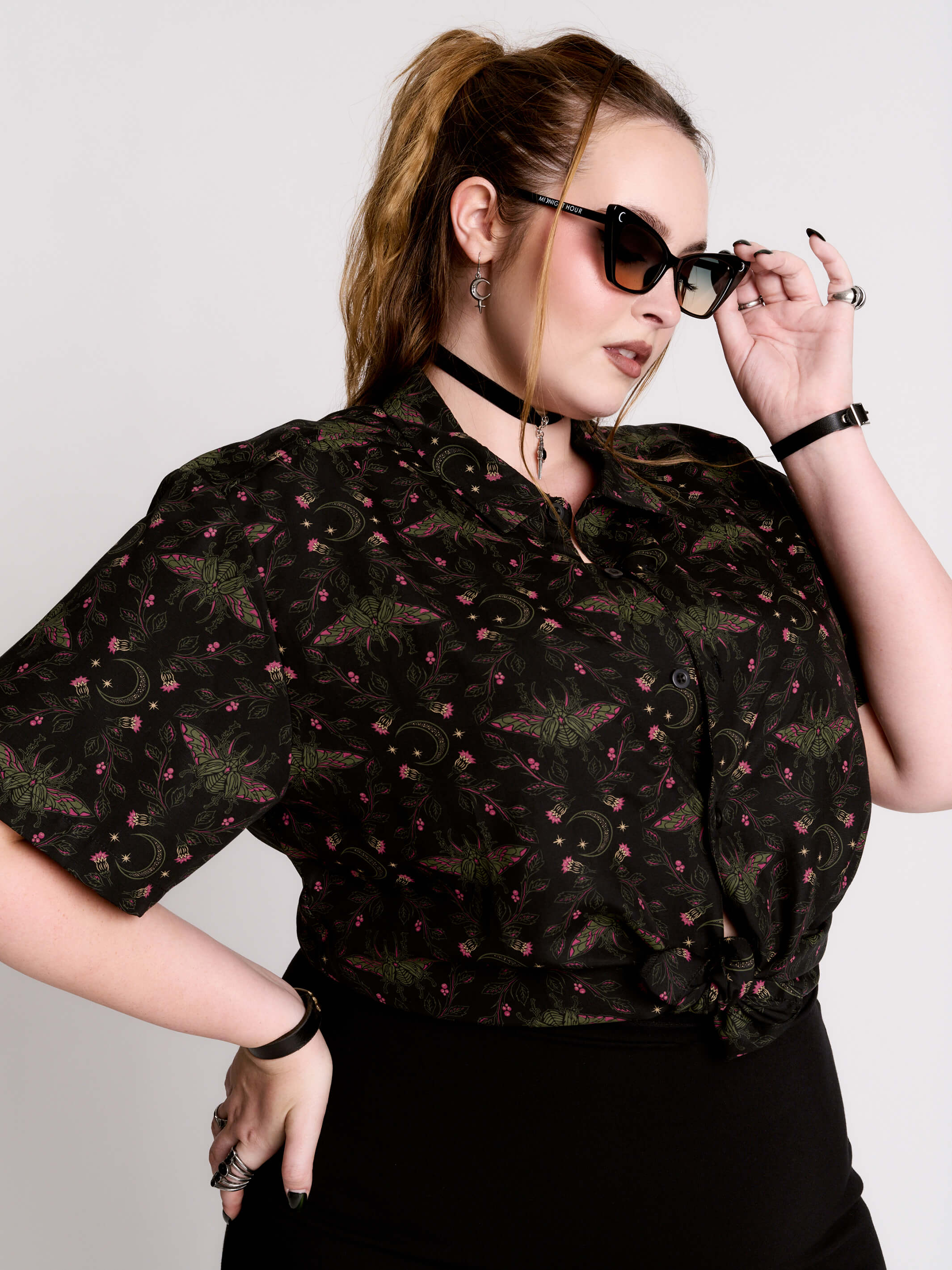 a black short-sleeve button-up shirt with a dark green and pink occult-style pattern.