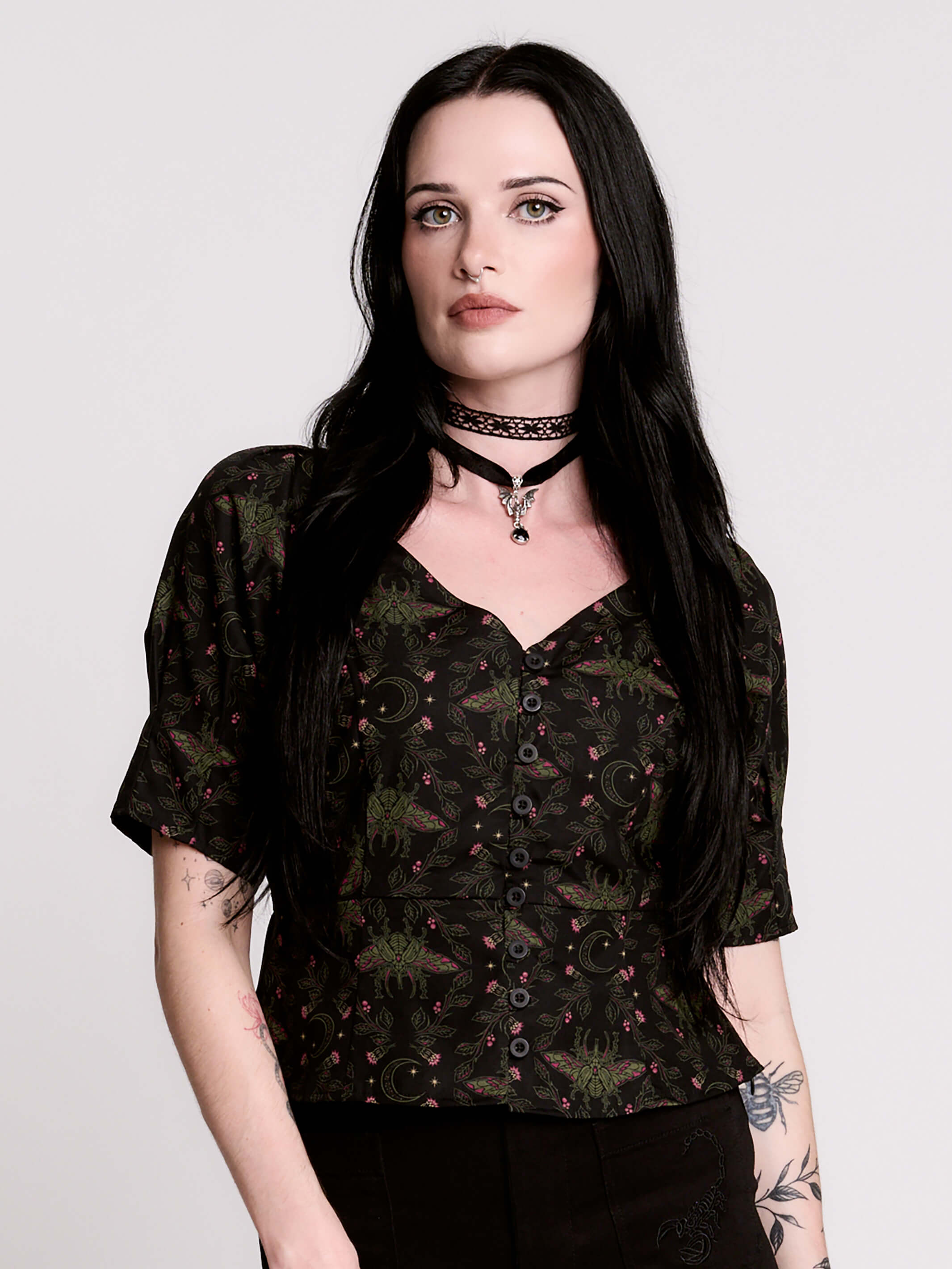 A short-sleeve button-up blouse featuring a dark green and black gothic pattern with pink accents.