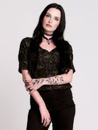 A short-sleeve button-up blouse featuring a dark green and black gothic pattern with pink accents.
