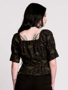 A short-sleeve button-up blouse featuring a dark green and black gothic pattern with pink accents.