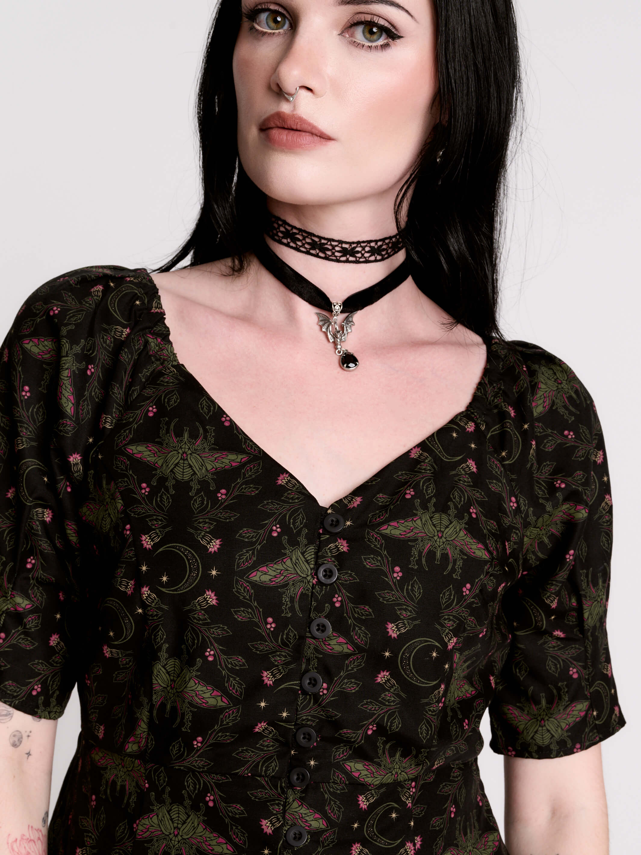 A short-sleeve button-up blouse featuring a dark green and black gothic pattern with pink accents.