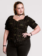 A short-sleeve button-up blouse featuring a dark green and black gothic pattern with pink accents.