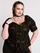 A short-sleeve button-up blouse featuring a dark green and black gothic pattern with pink accents.