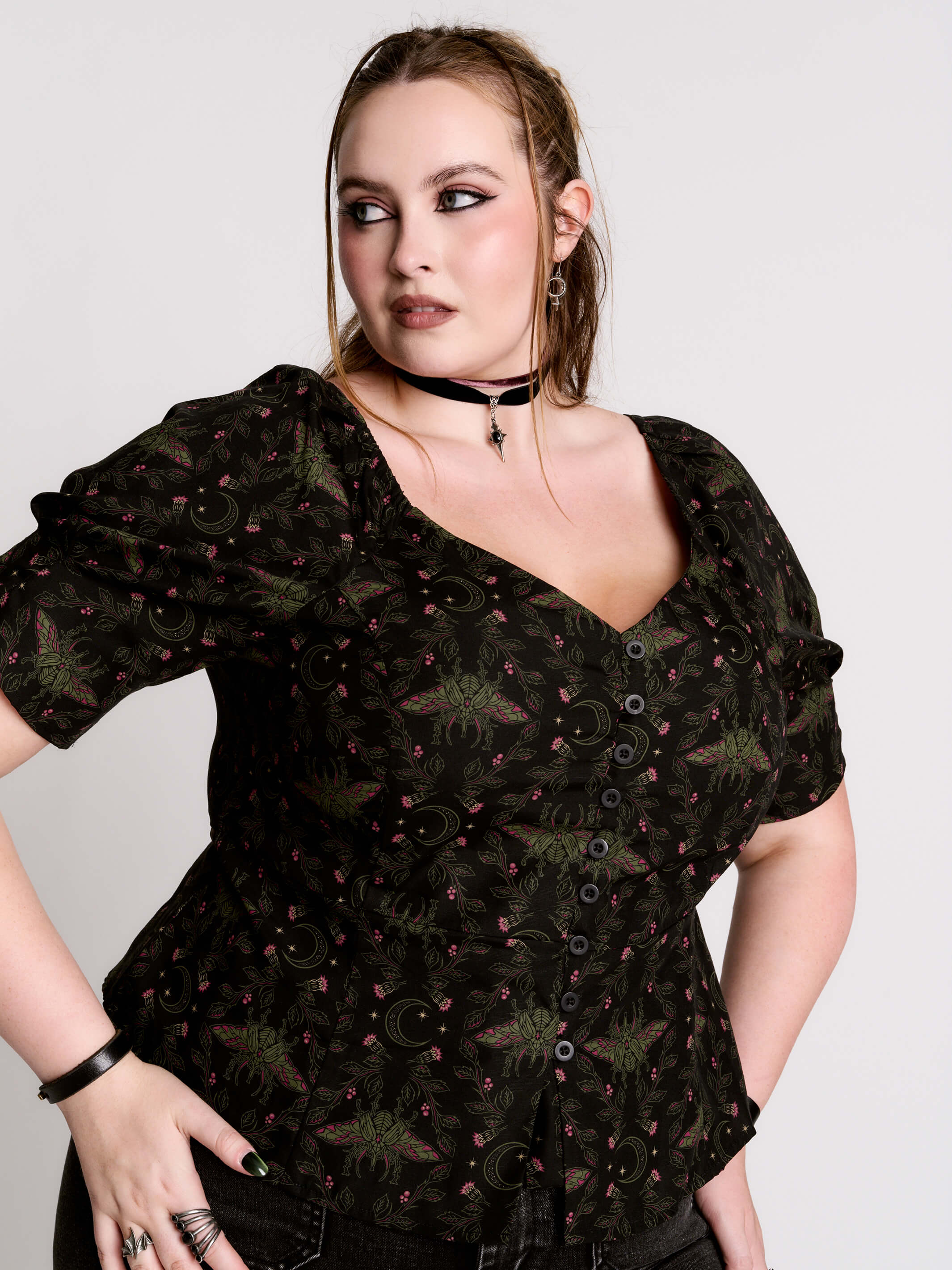 A short-sleeve button-up blouse featuring a dark green and black gothic pattern with pink accents.