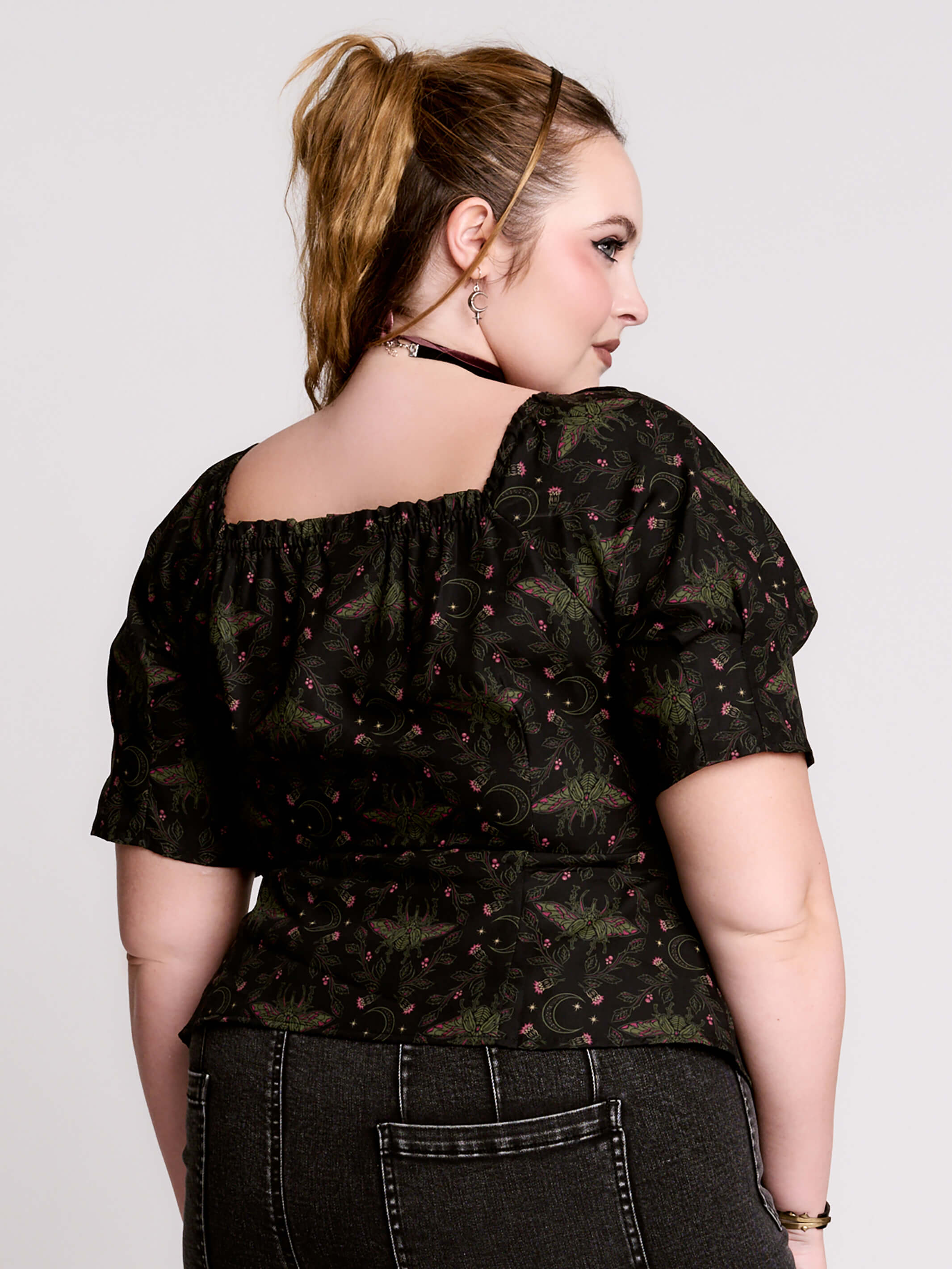 A short-sleeve button-up blouse featuring a dark green and black gothic pattern with pink accents.