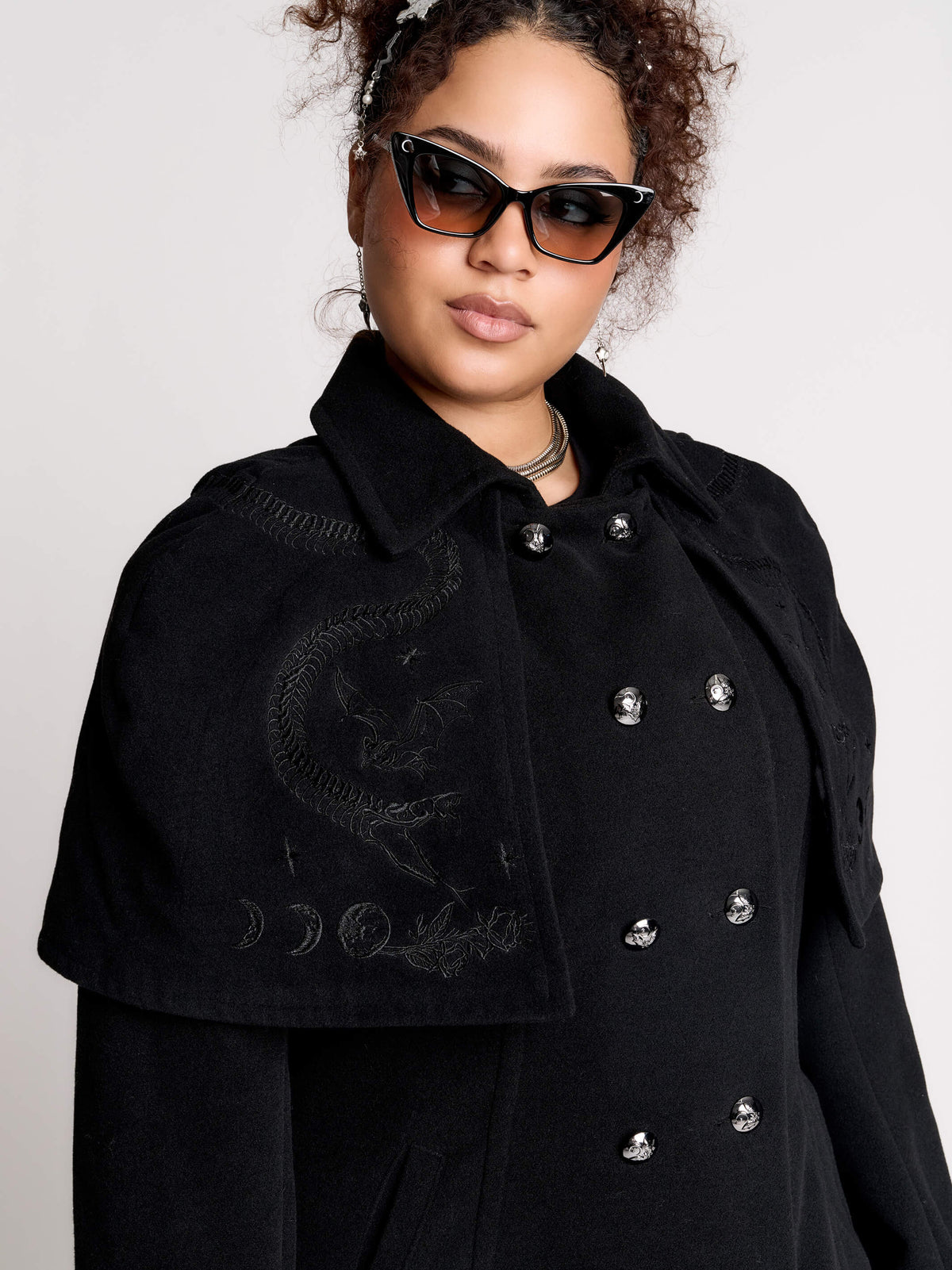 a black double-breasted coat with silver buttons and gothic dragon embroidery on the shoulder cape